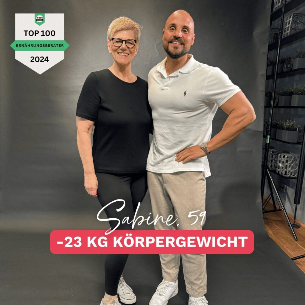 Sabine, 59 Jahre alt, strahlt nach ihrer beeindruckenden Gewichtsabnahme von 23 kg in den Wechseljahren. Sie trägt schwarze Sportbekleidung und posiert selbstbewusst neben ihrem Ernährungsberater. Im Bildhintergrund ist ein professionelles Studio-Setup zu sehen. Thema: Gewichtsabnahme Wechseljahre.