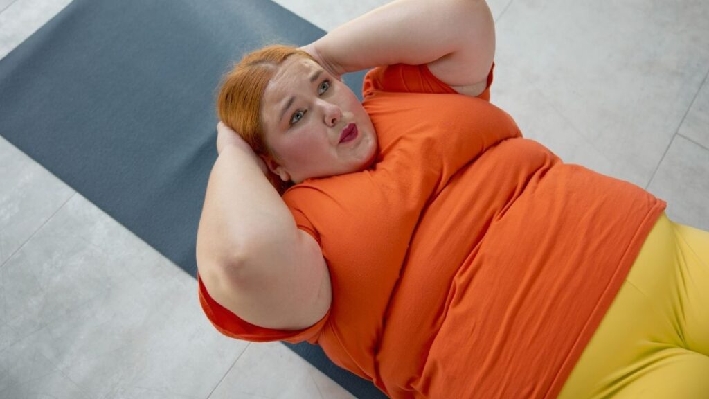 Frau versucht Crunches auf einer Fitnessmatte – sichtbar erschwert durch Fett am Bauch, das das Training unangenehm macht