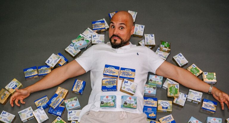 Coach Andreas Kotte liegt lachend in einem Meer aus Butterpäckchen – humorvolle Darstellung des Themas Fette in der Ernährung, Bauchfett Frau